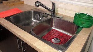 A kitchen with two stainless steel sinks, a wooden cutting board, and a green basket. - The Rameau 1er (Montréal)