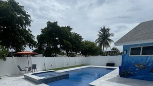 Una piscina con solárium empinado, un área de descanso con sillas azules y un mural en la pared contigua.