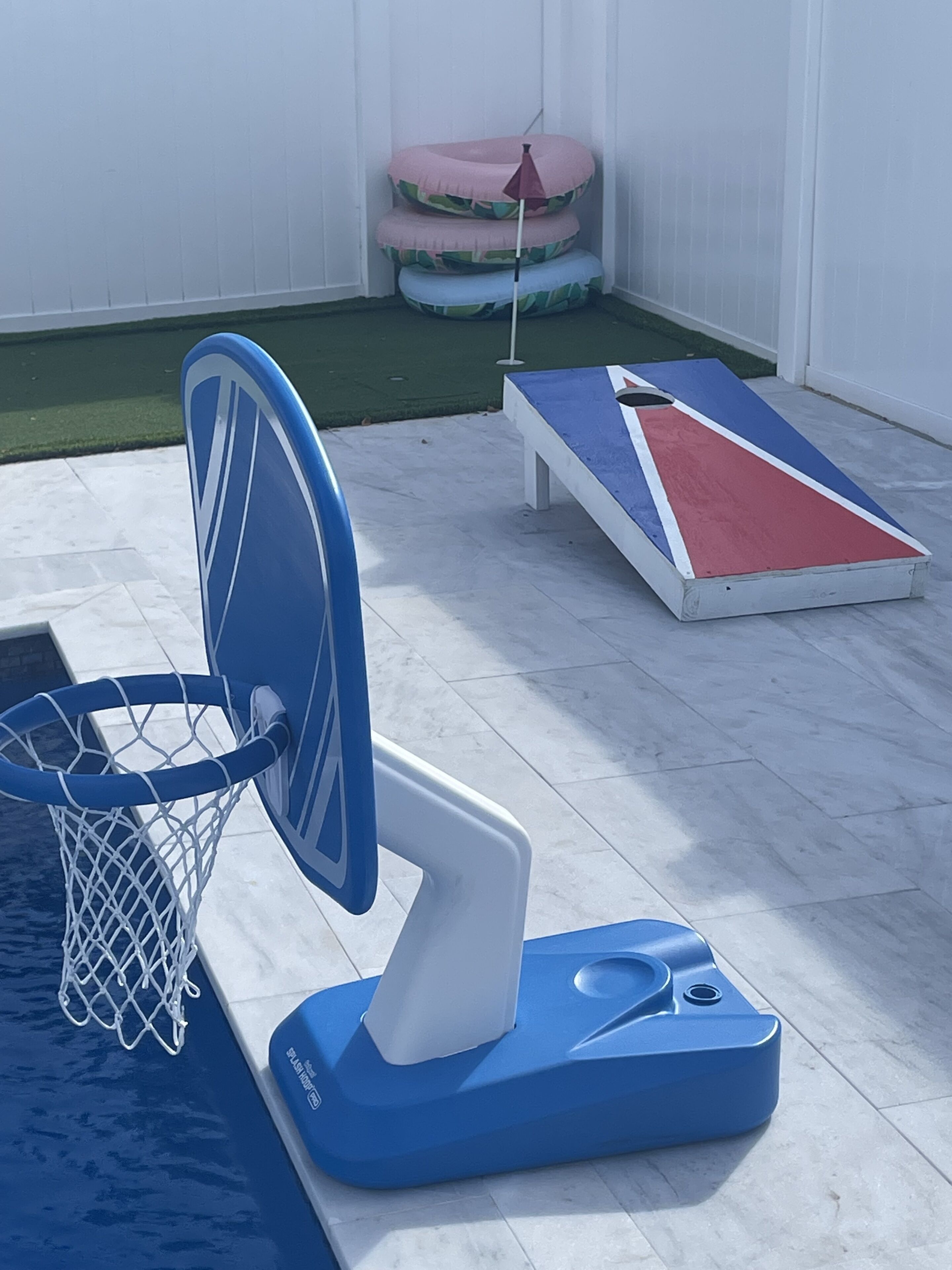 Et poolområde med et blå og hvidt poolbord, en lille oppustelig pool og en min basketkurv.