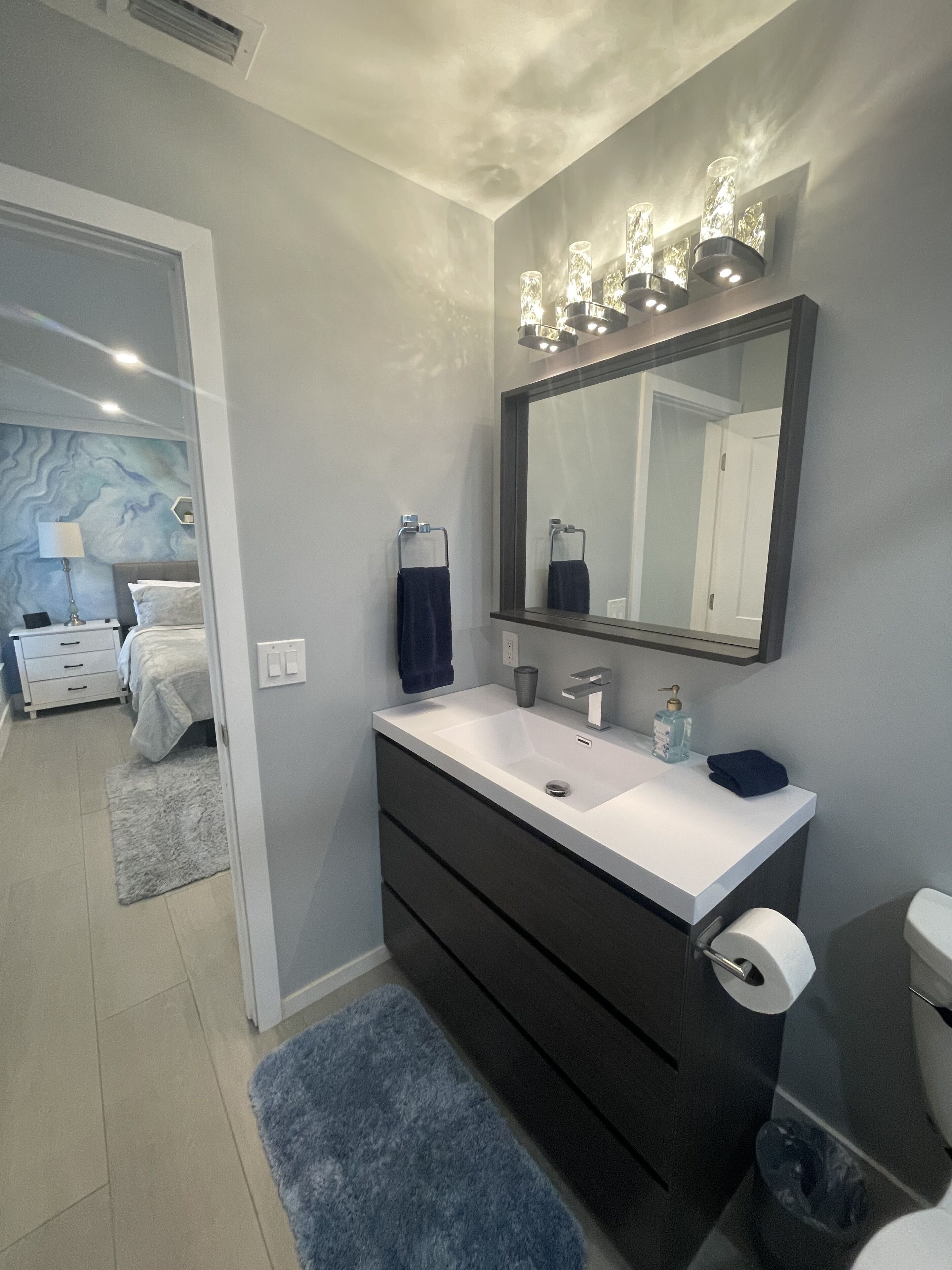 Une salle de bain moderne avec un grand miroir, un lavabo blanc et un meuble-lavabo foncé.