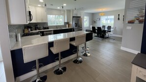 Una cocina moderna con una isla central, taburetes de bar y un comedor con candelabro.
