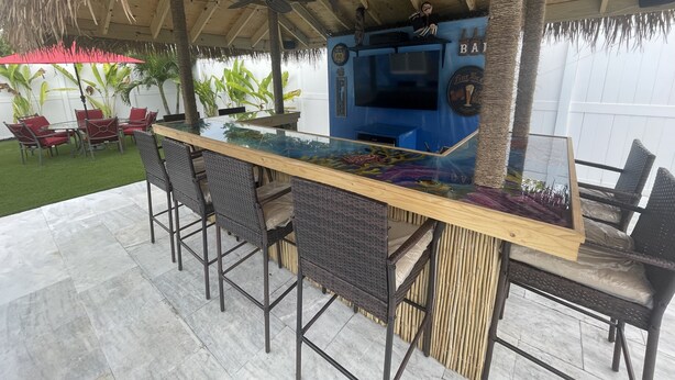Un área de bar al aire libre con una mesa de vidrio, sillas de mimbre y un ventilador de techo.