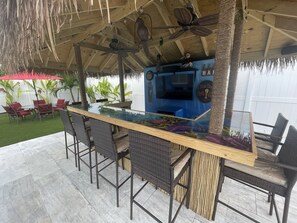 An outdoor bar area with a glass-top table, wicker chairs, and a ceiling fan. - Ocean Reef Paradise, Big Pool, Spa, Tiki Bar, Golf (Delray Beach)