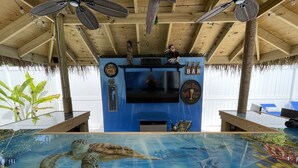 Un área de bar con un acuario grande, ventiladores de techo y una pantalla de televisión.