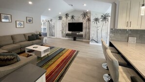Una sala de estar moderna con un sofá, una mesa de centro, televisor y una zona de cocina con armarios y encimera.