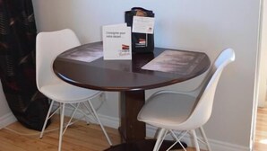 A round dining table with two white chairs, a black box, and a sign on the table. - Le Citadin (Rouyn-Noranda)