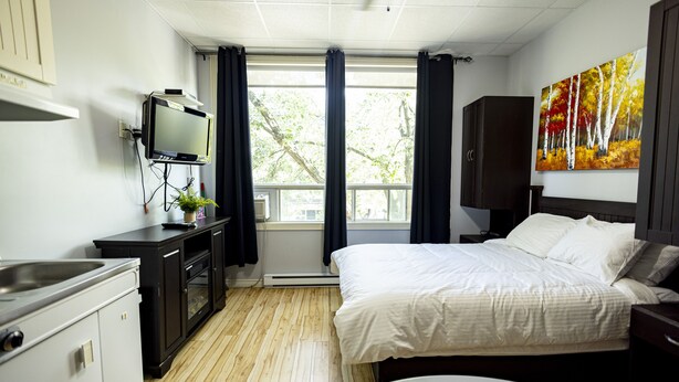 A hotel room with a bed, a TV, a desk, and a window with curtains. - Le Citadin (Rouyn-Noranda)