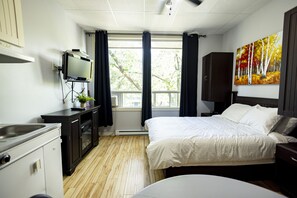 A hotel room with a bed, a TV, a desk, and a window with curtains. - Le Citadin (Rouyn-Noranda)