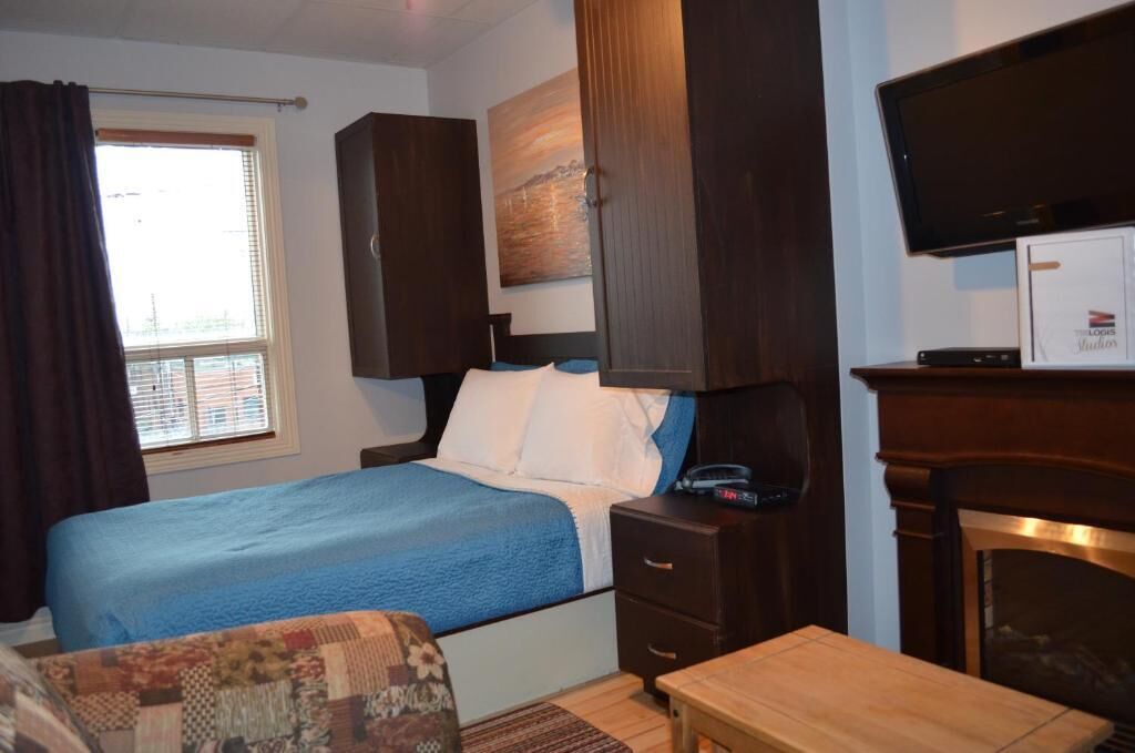 A bedroom with a bed, a desk, a television, and a fireplace.