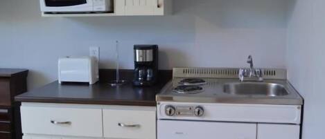 Eine kompakte Küche mit weißen Schränken, einer Mikrowelle, einem Toaster, einer Kaffeemaschine und einem Herd.