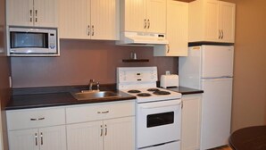 A compact kitchen with white cabinets, a microwave, a stove, and a refrigerator. - Le Citadin (Rouyn-Noranda)