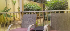 Un balcon avec deux fauteuils en osier et une table, entouré de plantes et adossé à un mur jaune.