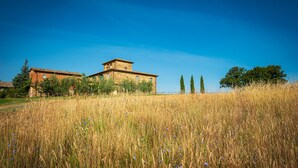 A rustic building with a prominent tower, surrounded by tall grass and trees. - Villa Gagnoni for 10p with private pool and large garden; airco in all bedrooms. (Sinalunga)