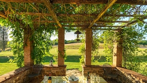 An outdoor dining area with a table set for two, surrounded by stone pillars and covered by a pergola. - Villa Gagnoni for 10p with private pool and large garden; airco in all bedrooms. (Sinalunga)