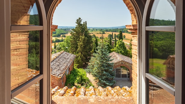 A room with a large arched window overlooking a courtyard with brick buildings and greenery. - Villa Gagnoni for 10p with private pool and large garden; airco in all bedrooms. (Sinalunga)