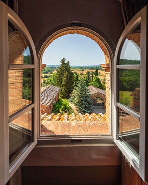 A room with a large arched window overlooking a courtyard with brick buildings and greenery.