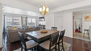 A spacious living area with a wooden dining table, comfortable seating, and a modern chandelier.