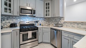A modern kitchen with grey cabinets, stainless steel appliances, and a tiled backsplash.