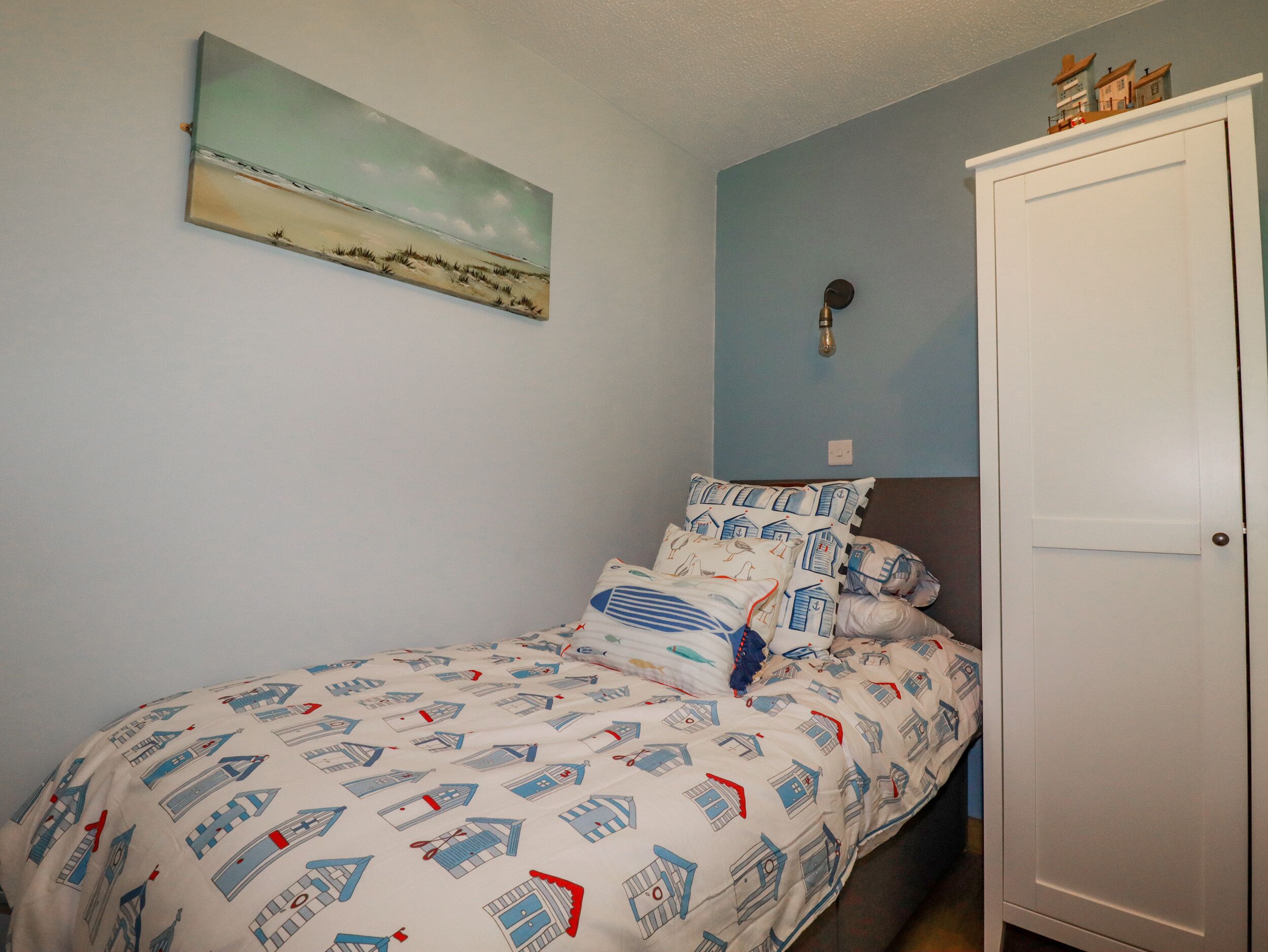 A bedroom with a bed, pillows, a wall-mounted painting, a light fixture, and a wardrobe.
