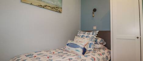 A bedroom with a bed, pillows, a wall-mounted painting, a light fixture, and a wardrobe.