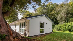 A white building with a sloped roof, large windows, and a door. - Woodside (Liskeard)