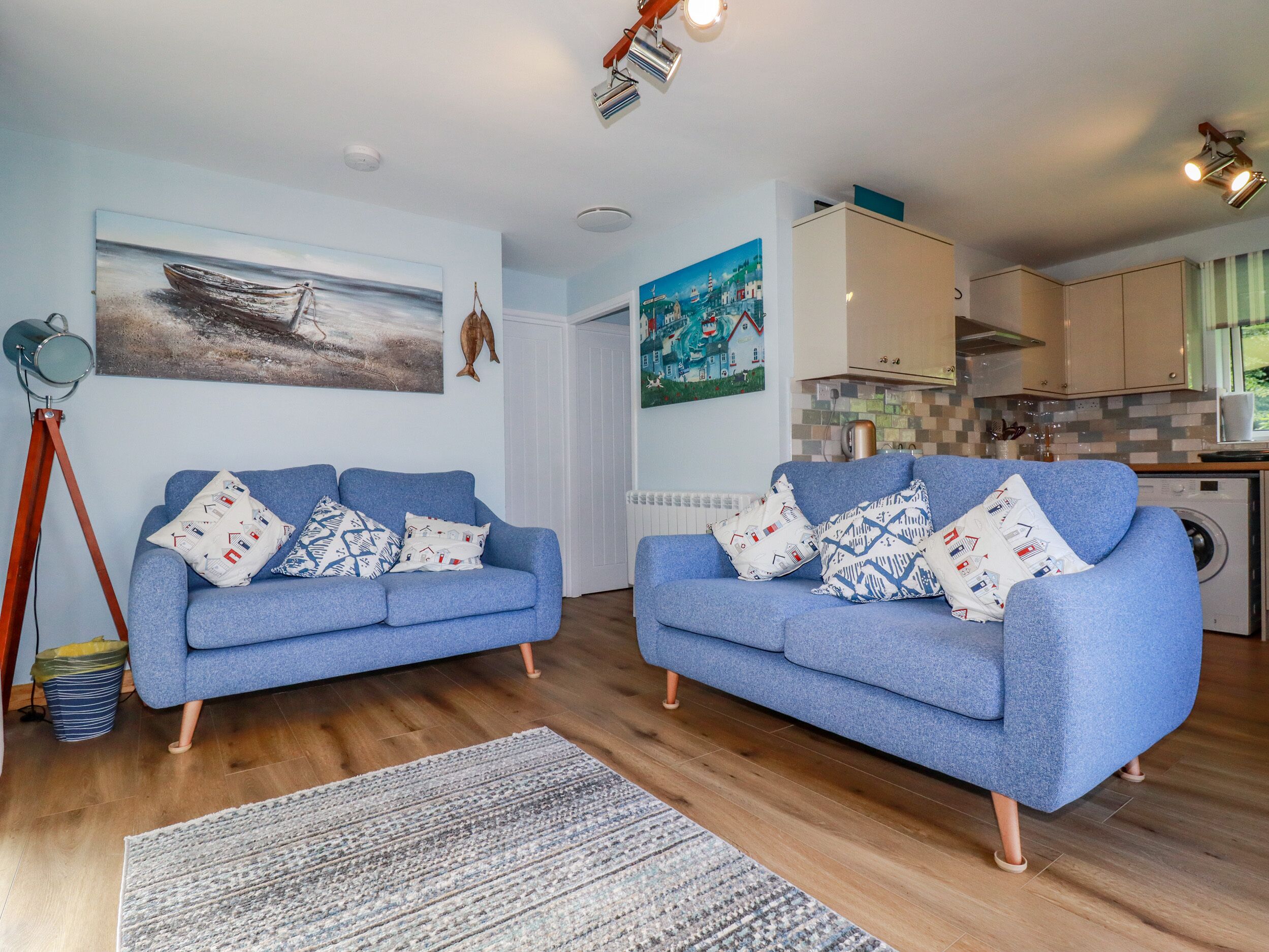 A living room with two blue sofas, a patterned rug, and a painting of a boat on the wall.