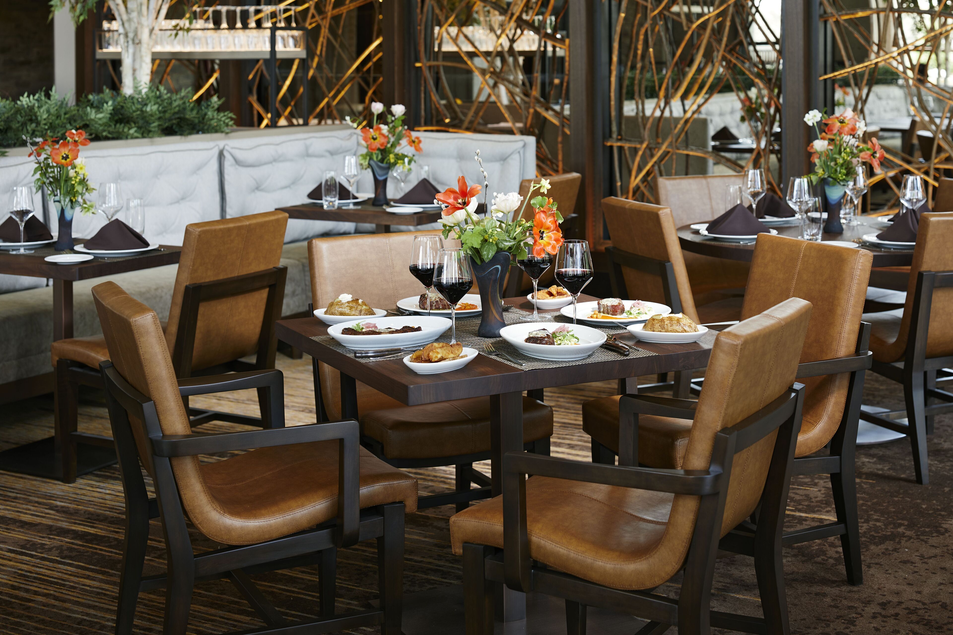 A restaurant setting with tables set for dining, featuring brown leather chairs and dark wood tables.