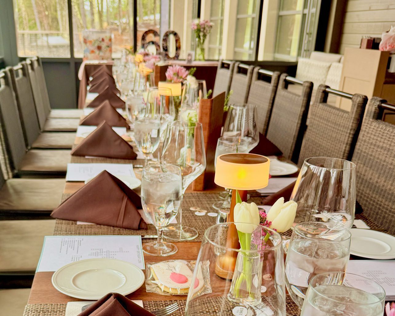 A dining table set with glassware, plates, and napkins, with a lamp and flowers on the table.