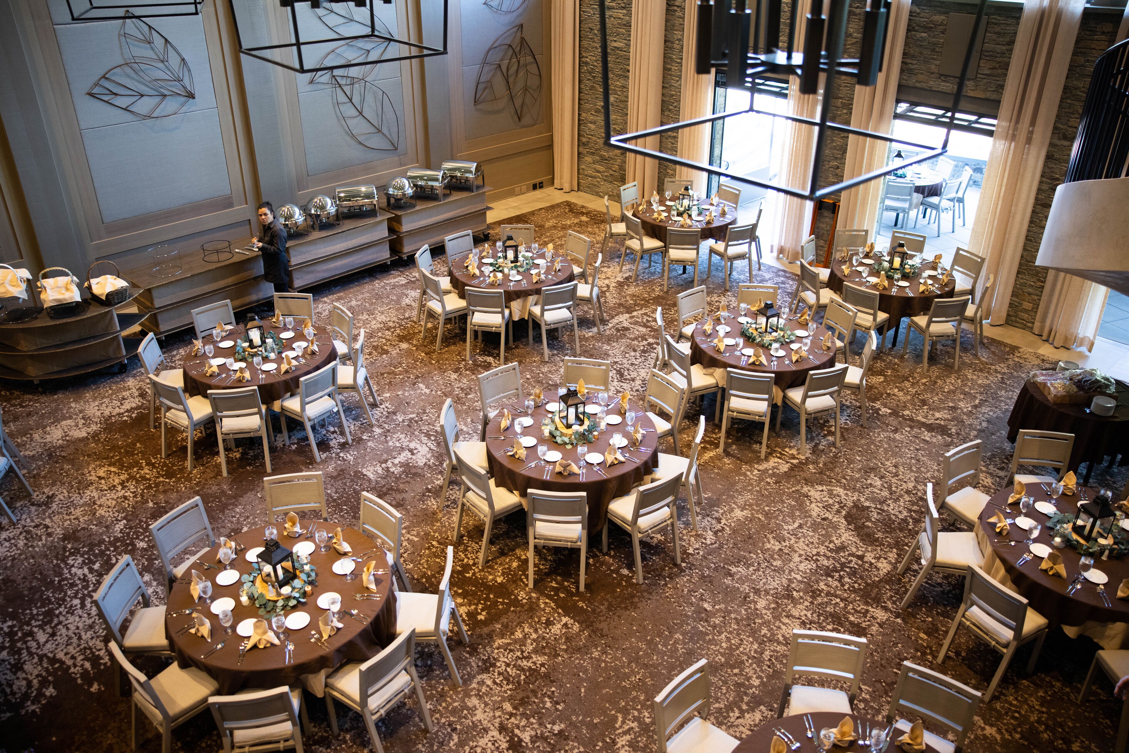 A hotel dining area with multiple round tables set for guests, featuring a carpeted floor and modern decor.