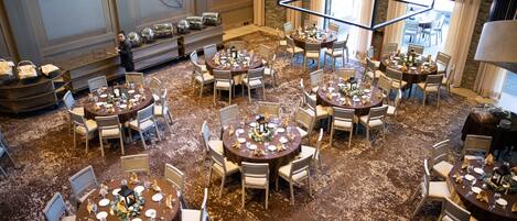 A hotel dining area with multiple round tables set for guests, featuring a carpeted floor and modern decor.