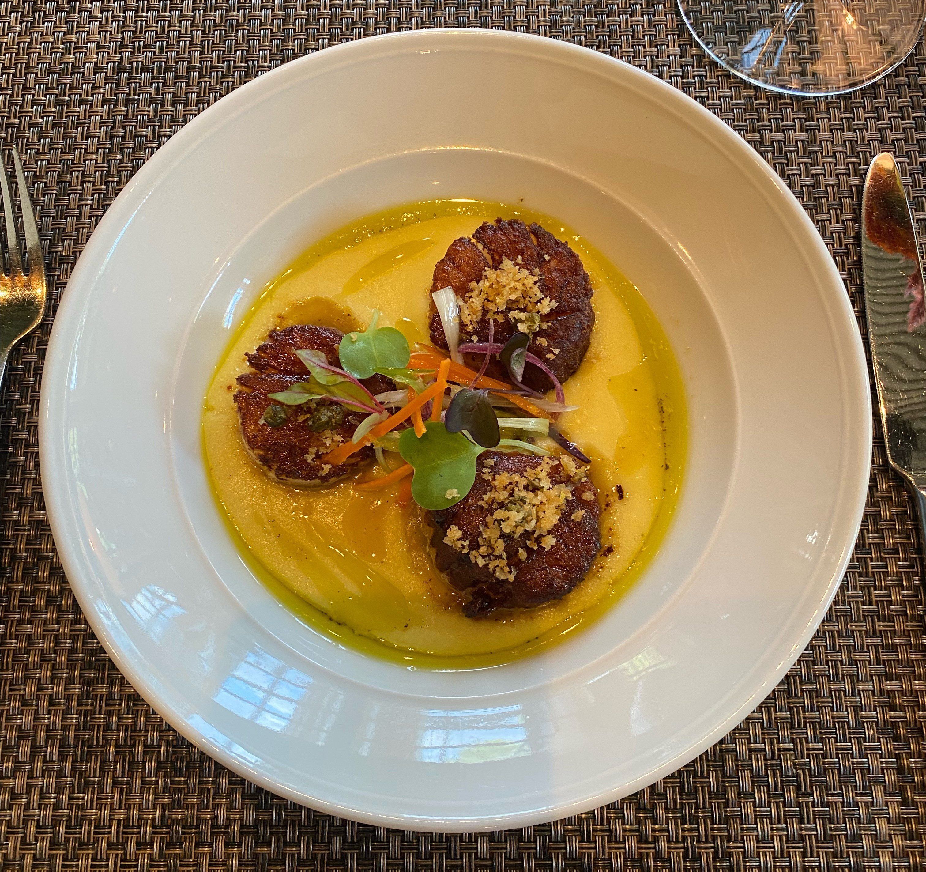 A white plate with a yellow sauce, two round meat items, and garnishes on a woven tablecloth.