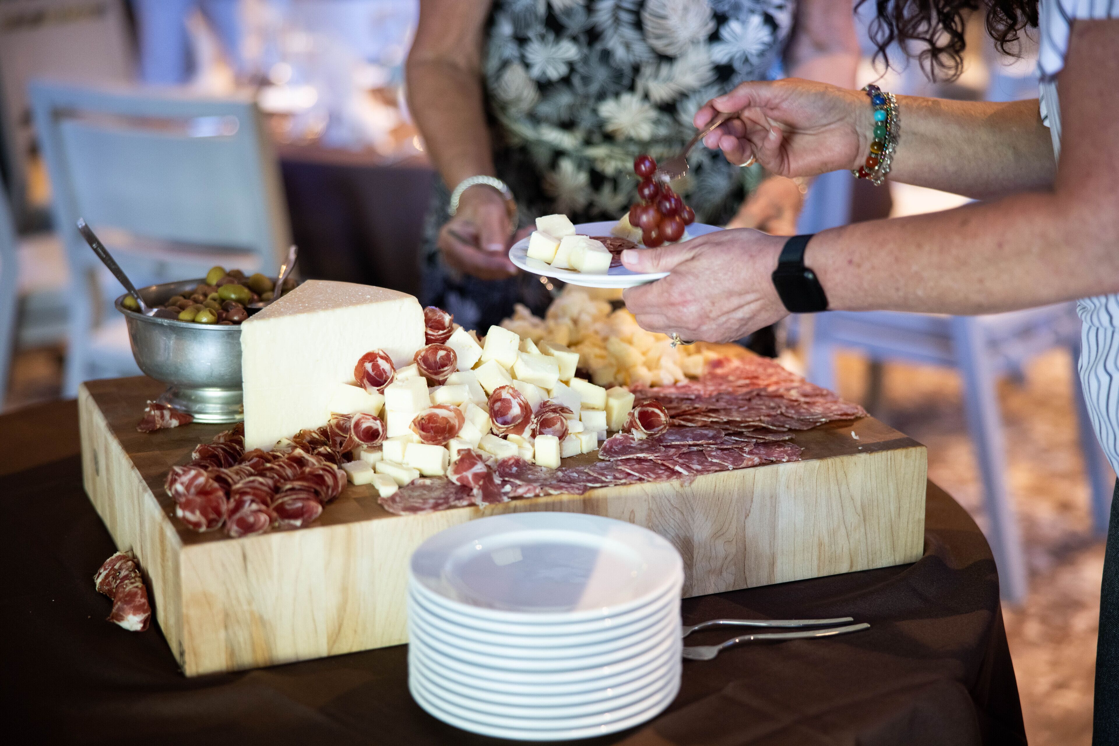 Une planche en bois garnie de différents fromages et de charcuteries, accompagnée d’un bol d’olives et d’une assiette de raisins.