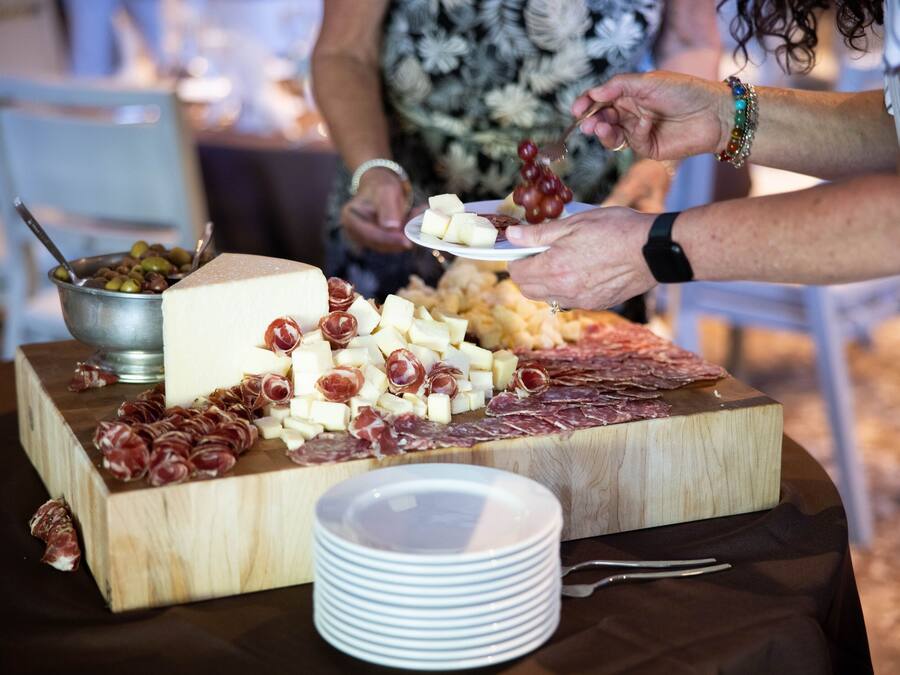 A wooden board with various cheeses and cured meats, accompanied by a bowl of olives and a plate of grapes.