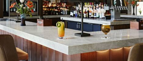 A bar area with a marble countertop, a vase with flowers, and two glasses of beverages.