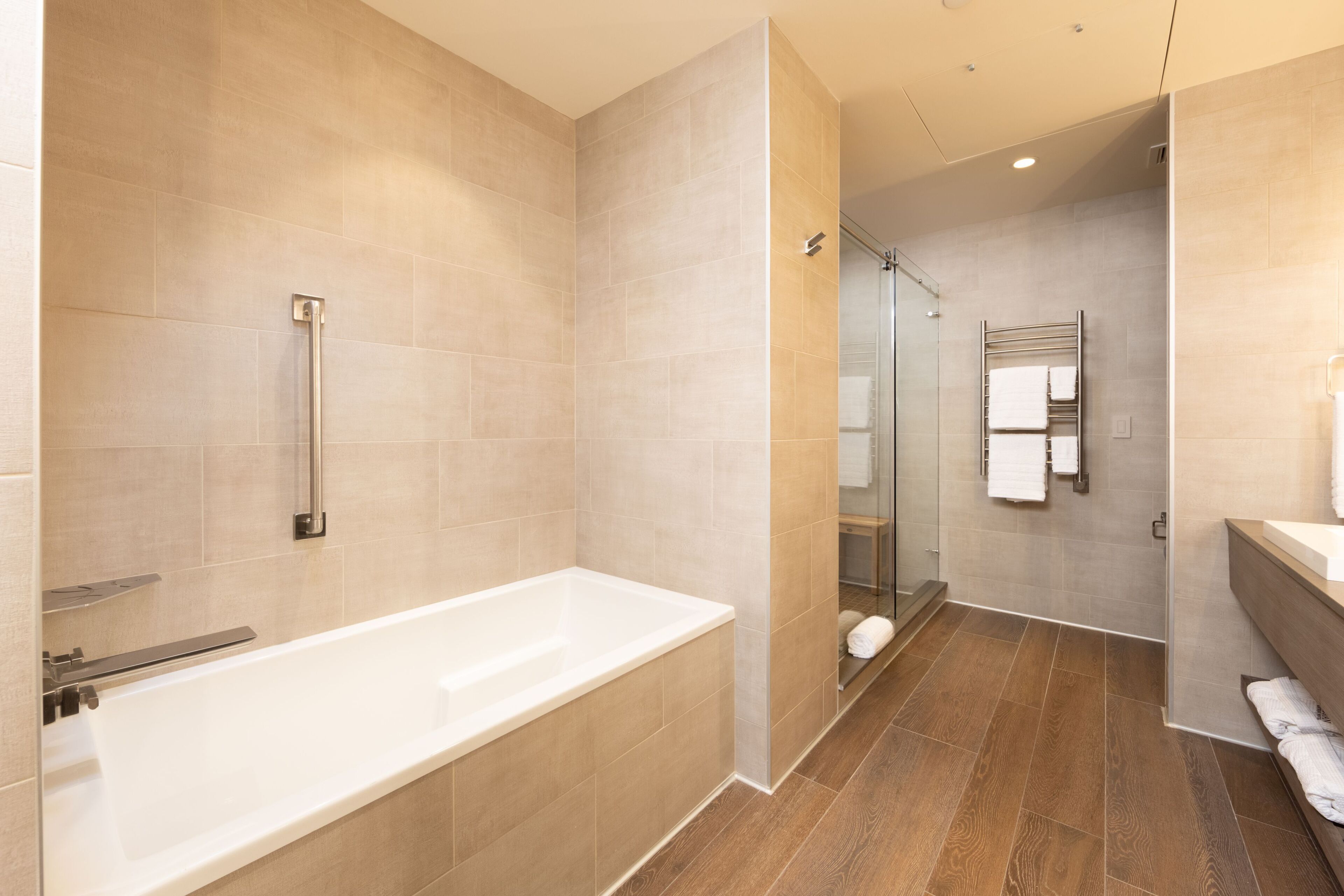 Une salle de bain moderne avec une grande baignoire, une douche à l’italienne avec des parois en verre et un plancher en bois.