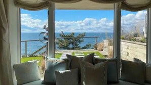 A room with a large window overlooking a scenic view of the sea and a garden. - Sunset Bluff: Breathtaking views of LI Sound. (Northport)