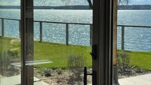 A view from a glass door to a lake with a metal railing and greenery. - Sunset Bluff: Breathtaking views of LI Sound. (Northport)