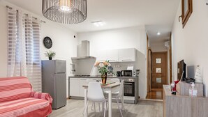 Une cuisine moderne avec des meubles blancs, un coin repas comprenant une table et des chaises blanches, un canapé rouge et une plante décorative.