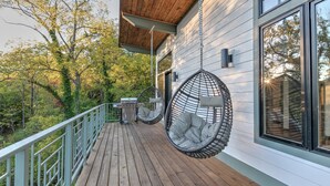 Une terrasse en bois avec des chaises suspendues et un barbecue, donnant sur une zone boisée.