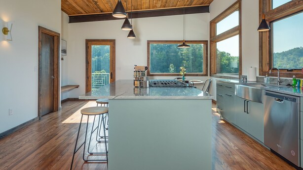 Une cuisine moderne dotée d’un îlot central, de grandes fenêtres et d’un plafond en bois.