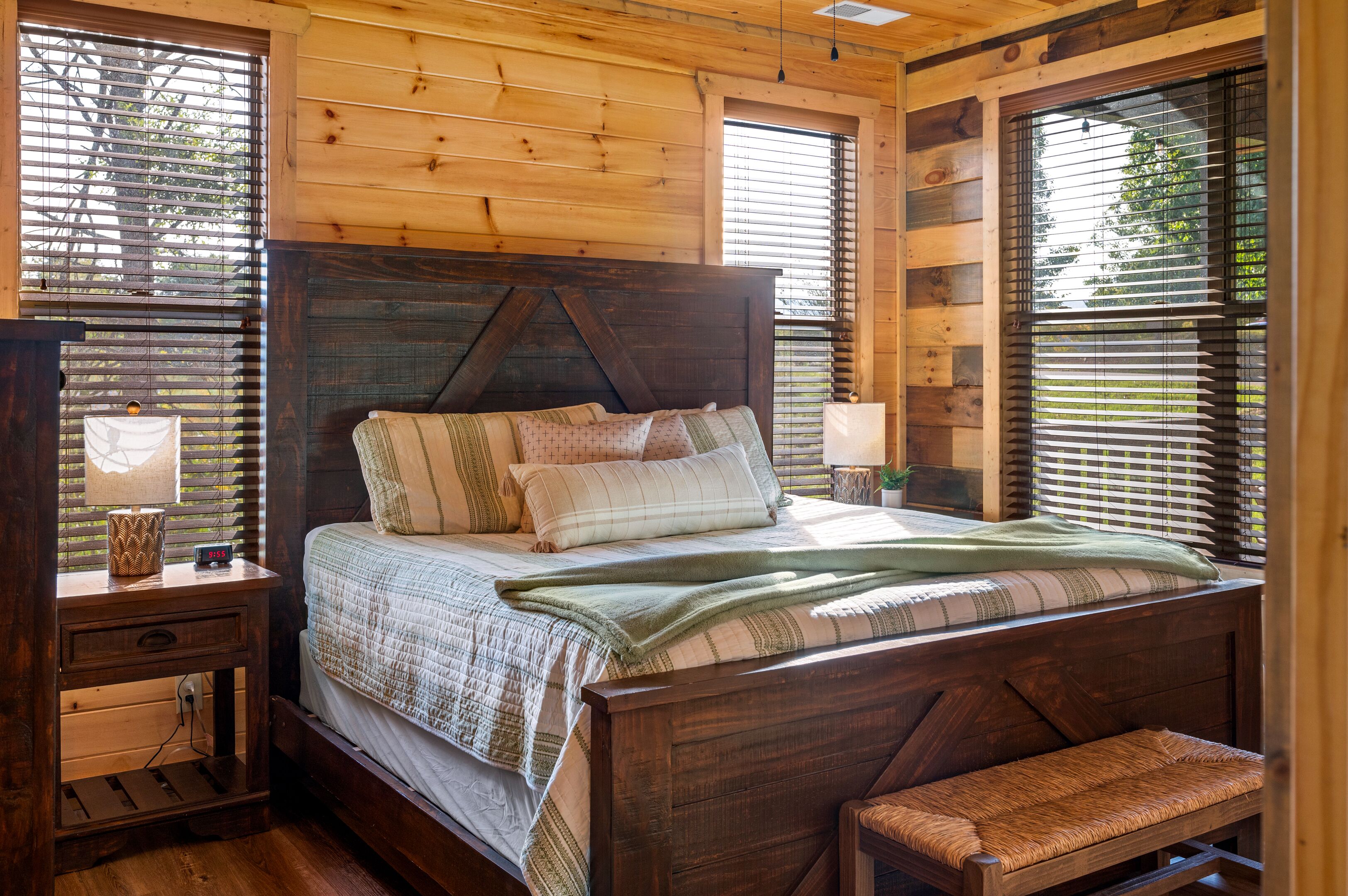 Une chambre dans une cabane en bois, avec un lit, une table de chevet, une lampe et un banc.