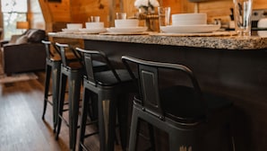A wooden interior with a bar area featuring black stools, a kitchen with dark cabinets, and pendant lighting. - Planning a Smokey Mtn Family Vacation? Stay Here! They will love you for it. (Sevierville)
