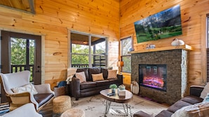 A cozy log cabin interior with a fireplace, comfortable seating, and a large TV mounted on the wall. - Planning a Smokey Mtn Family Vacation? Stay Here! They will love you for it. (Sevierville)