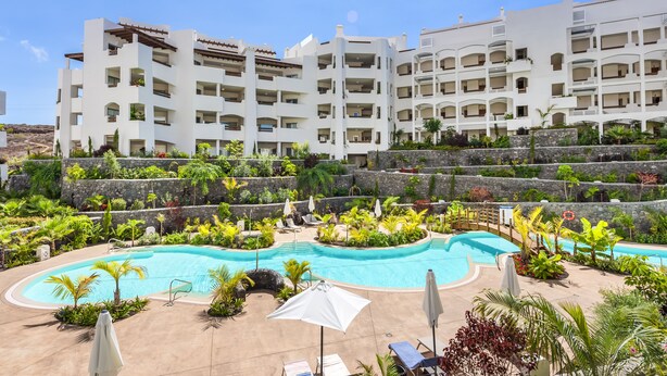 A resort with a swimming pool surrounded by lush greenery and a multi-story building with balconies. - MAGNIFICENT NEW APARTMENT ADAMA JARDINES DE LOS MENCEYES (Palm-Mar)