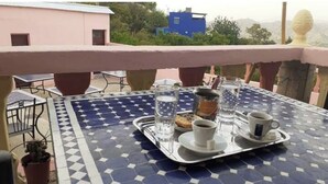 A dining table with a tray containing a cup of coffee, a glass of water, and a pastry, set against a blue and white tiled floor.