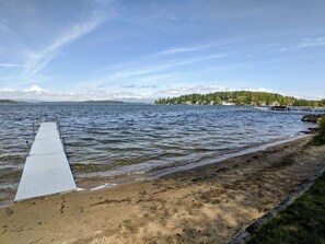 Walk along the lakeside path to a tranquil dock area surrounded by a sandy shoreline and lush forest.