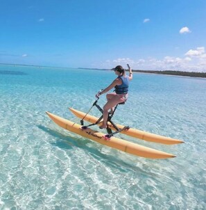 Une personne fait de la planche à pagaie sur une mer turquoise et limpide, avec une côte visible au loin.