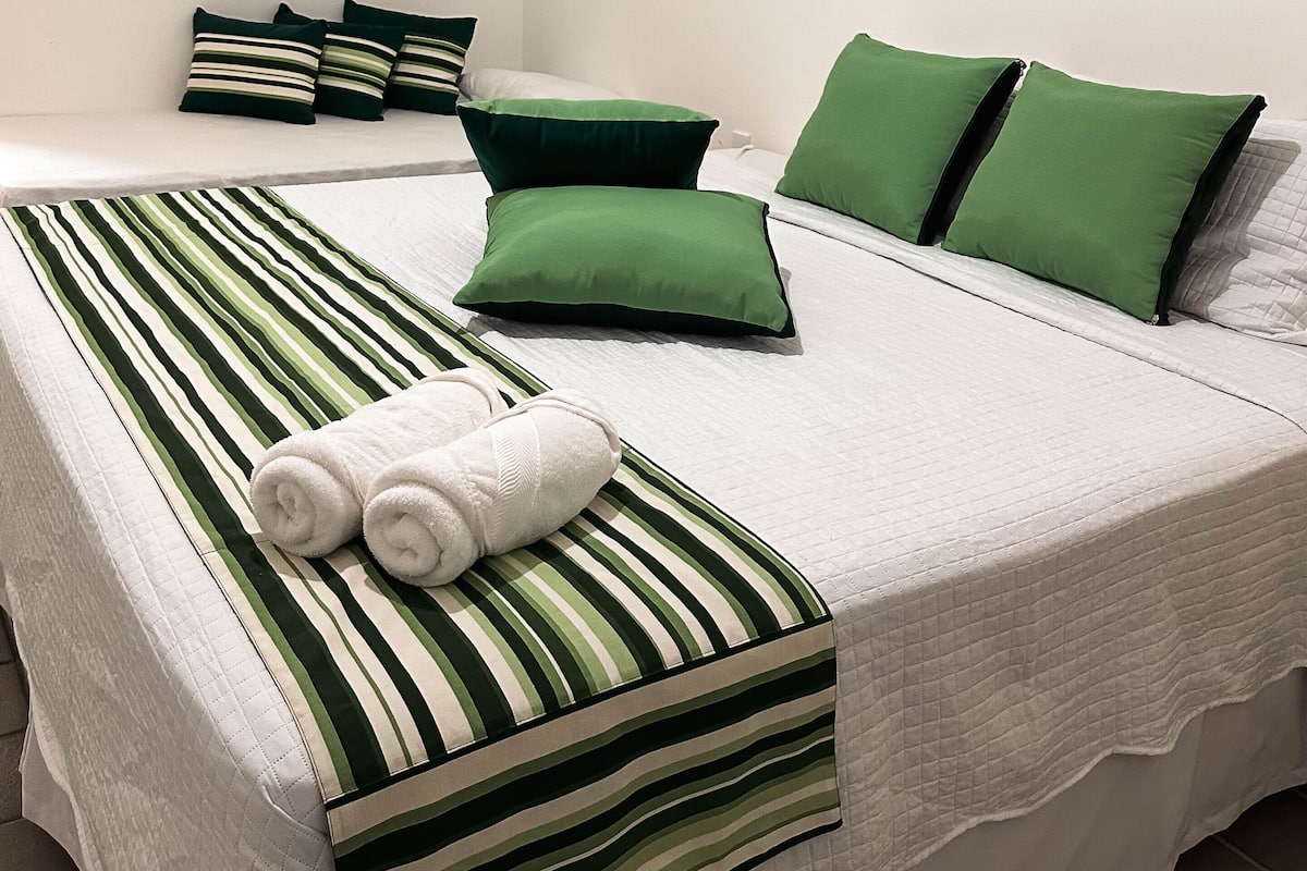 A hotel room with two beds, each with green and white striped bedding and matching pillows.