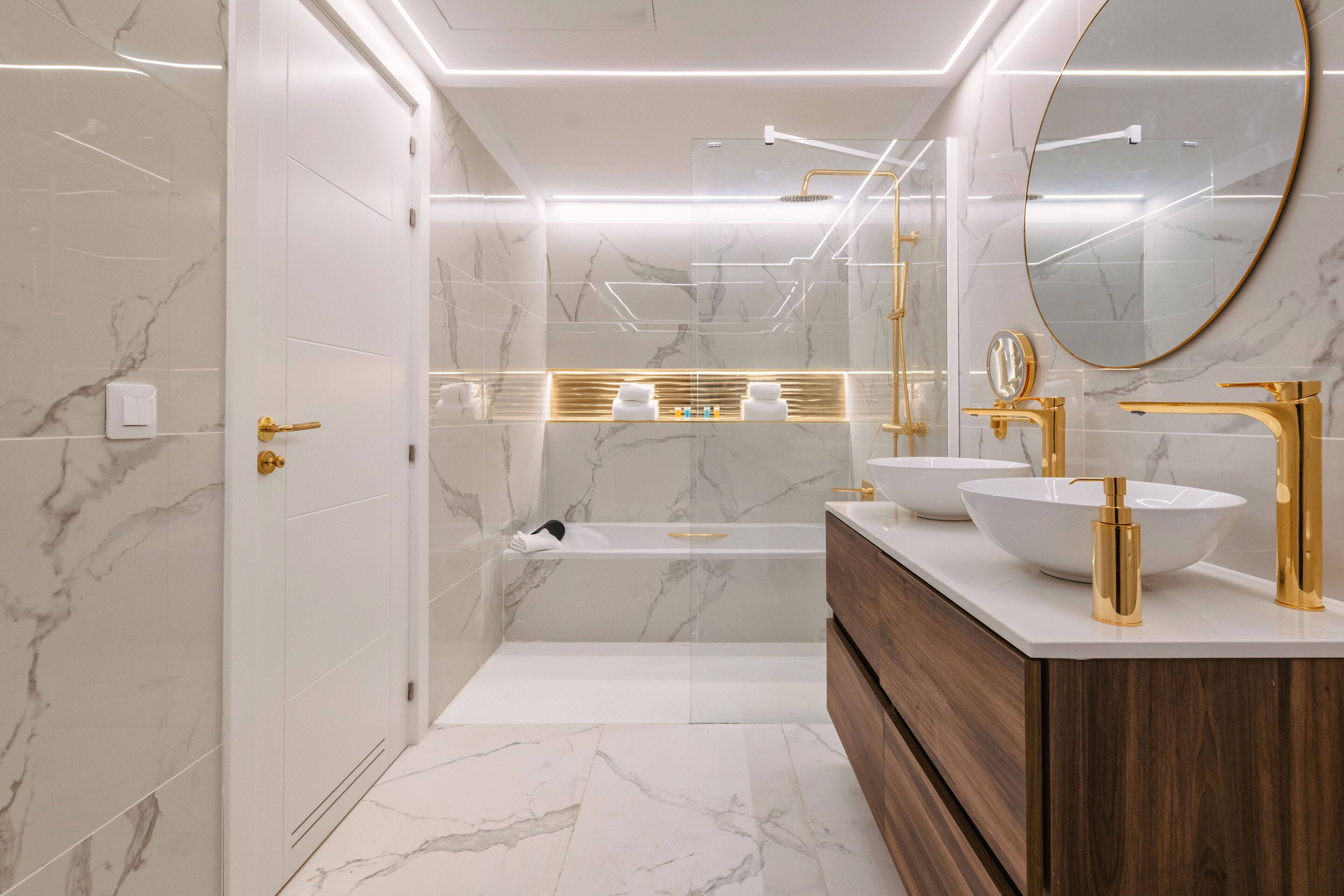 A modern bathroom with marble walls, a bathtub, and gold fixtures.