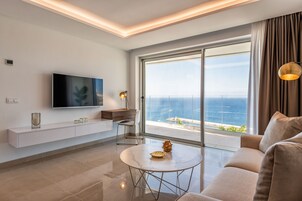 Un soggiorno moderno con un televisore grande, un divano, un tavolino da caffè e vista sull'oceano attraverso ampie finestre.